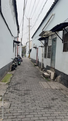Suzhou, China, 31 March 2026 - Narrow cobblestone alley flanked by whitewashed walls and traditional tiled rooftops in an old residential hutong neighborhood in spring.