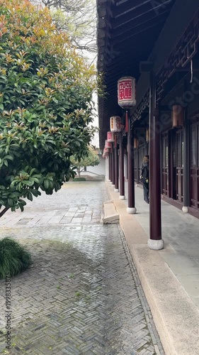 Suzhou, China, 31 March 2026 - A woman strolls along a traditional Chinese corridor with red pillars and decorative lanterns in a classical garden in spring.