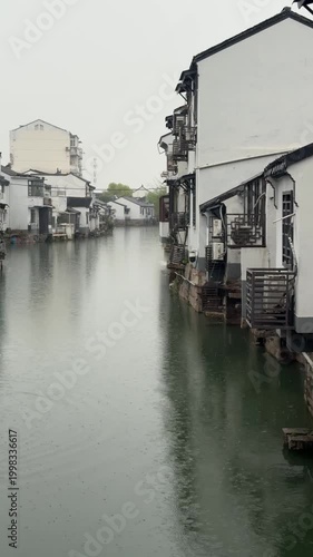 Suzhou, China, 31 March 2026 ? Rain falls on a tranquil canal lined with traditional whitewashed Jiangnan-style water houses on a misty spring day.