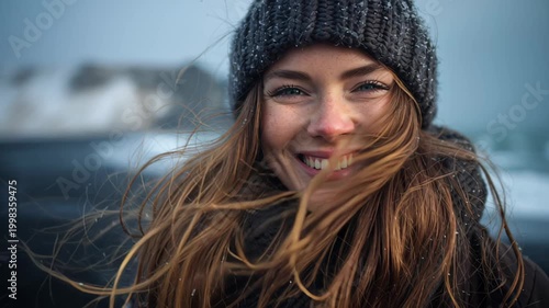 Close-up footage of a young woman wearing a warm knitted beanie in cold weather, hair blowing in the wind with snowflakes, winter outdoor lifestyle concept