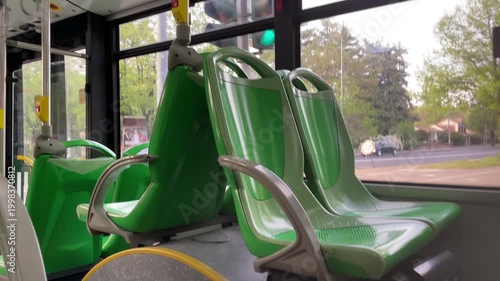 Bus Seats: Modern bus interior with empty green seats near window with natural daylight and trees in background.