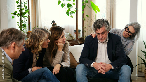Foto Family members supporting a sad senior man during a difficult time at home