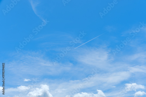 鮮やかな青空を斜めに横切る一筋の飛行機雲と白く広がる雲の風景。広大な空の余白を活かしたコピースペースのある背景素材。