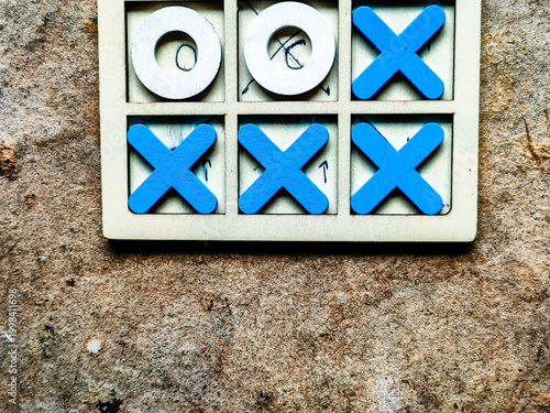 Top view of wooden tic-tac-toe game pieces (Xs and Os) on a rustic concrete surface.