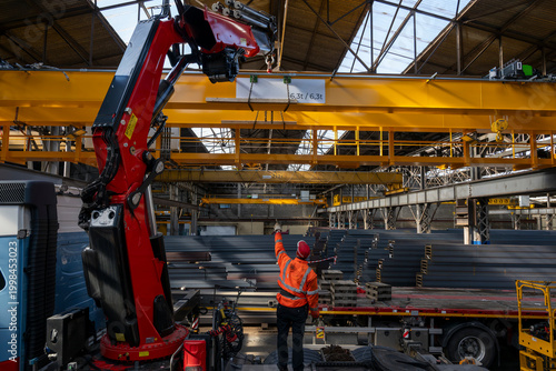 Foto Industrial worker guiding overhead crane and red truck mounted lifting arm while