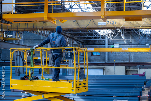 Obraz na plátně Industrial worker standing on elevated yellow scissor lift platform inside wareh