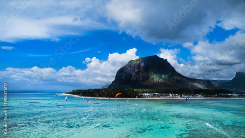 Bild auf Leinwand Kitesurfers glide across the crystal turquoise lagoon of Le Morne beach, Mauritius, with the iconic UNESCO-listed Le Morne Brabant mountain rising dramatically behind