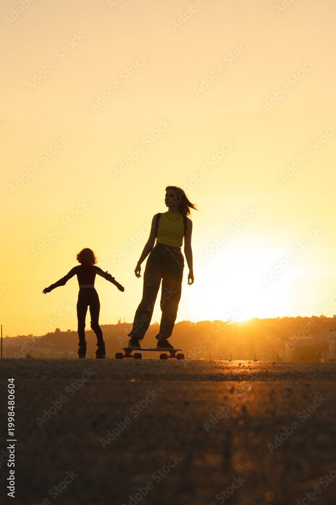 Fototapeta premium Young women longboarding and rollerblading at sunset