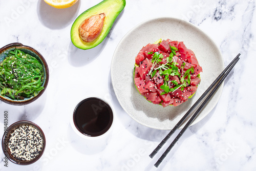 Fresh tuna tartare with avocado served on a marble table with soy sauce and seaweed salad