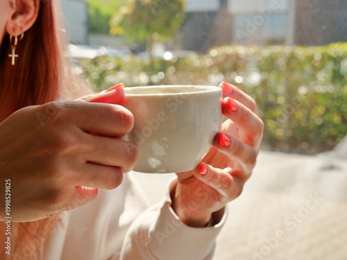 Photos person's hands holding a warm white ceramic cup in bright natural sunlight