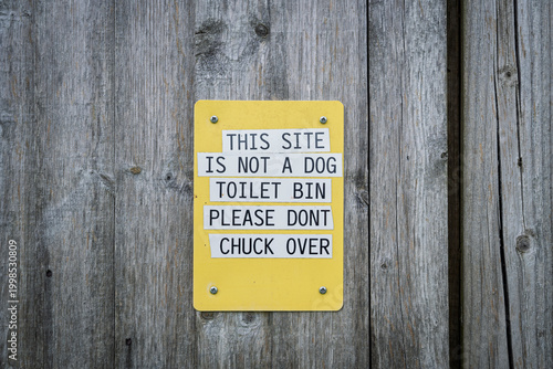 Yellow Warning Sign On Wooden Fence Asking People Not To Use Site As Dog Toilet Bin