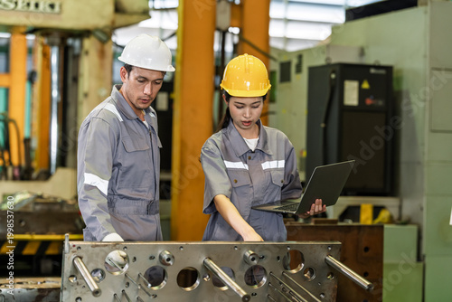 Принти на полотні Asian adult female engineer points at metal component while caucasian adult male colleague holds laptop, reviewing part quality, process detail and production data in connected factory workshop