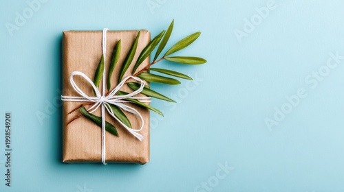 Rectangular present wrapped in brown paper and adorned with natural foliage rests on a light blue surface