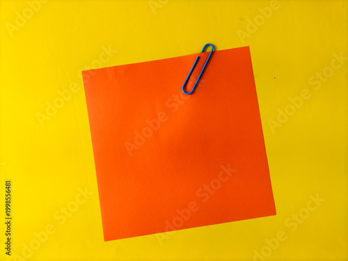 Orange square paper clipped with a blue paperclip on a vibrant yellow background. 