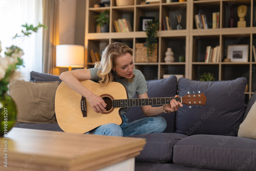 Obraz premium Woman playing acoustic guitar and singing on sofa