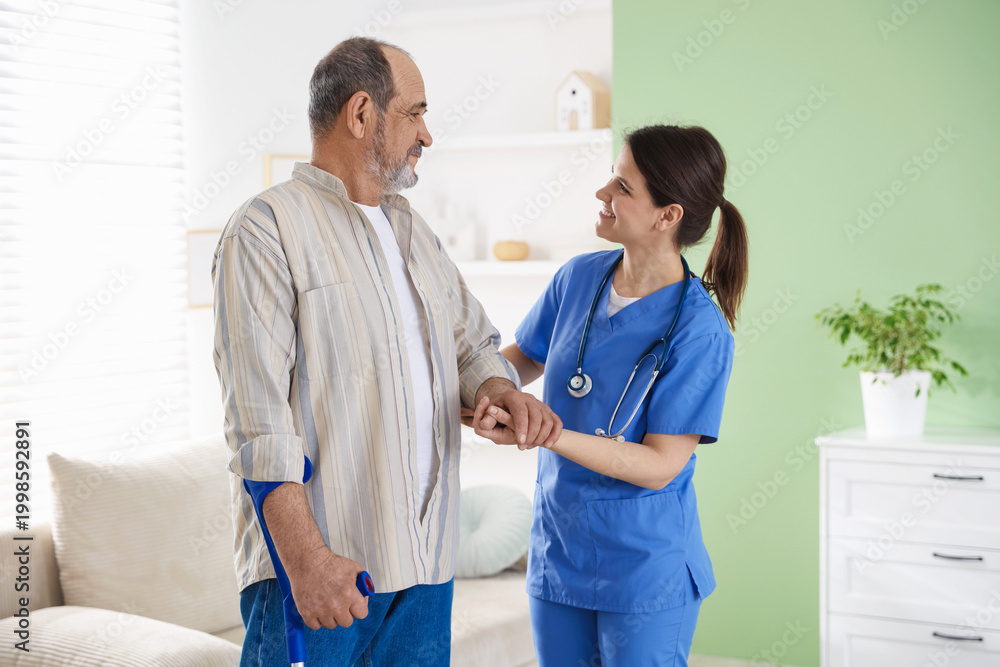 Fototapeta premium Smiling care worker supporting senior man at nursing home