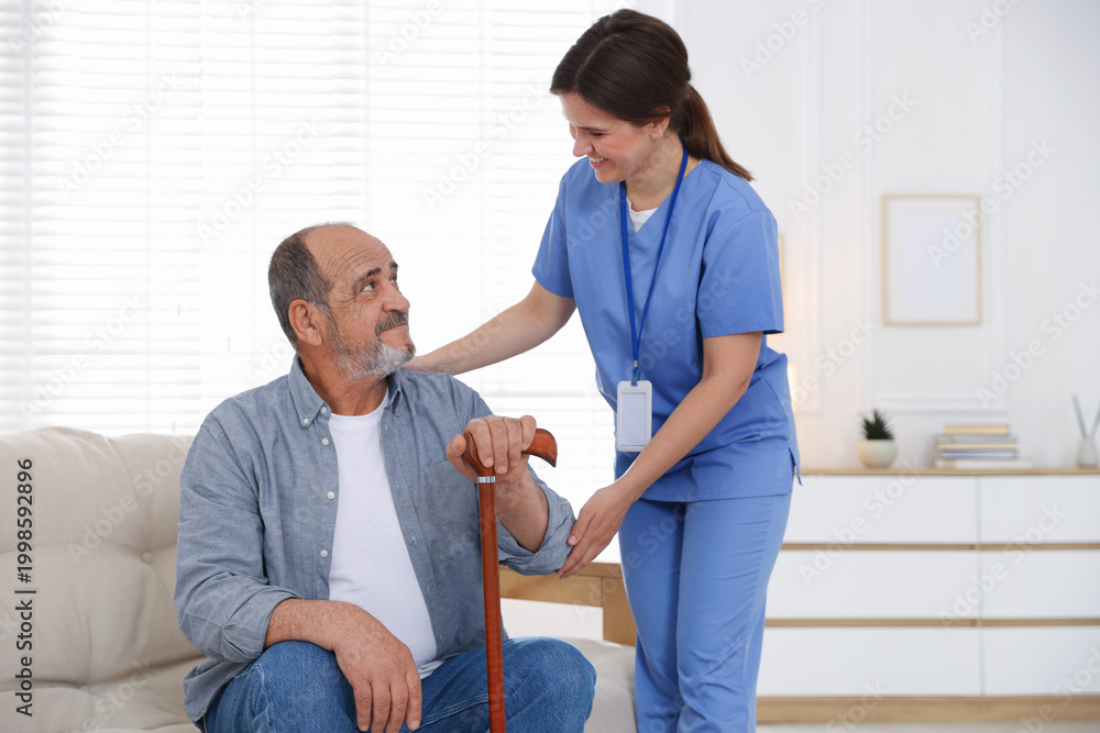 Obraz premium Smiling care worker supporting senior man with walking cane at nursing home