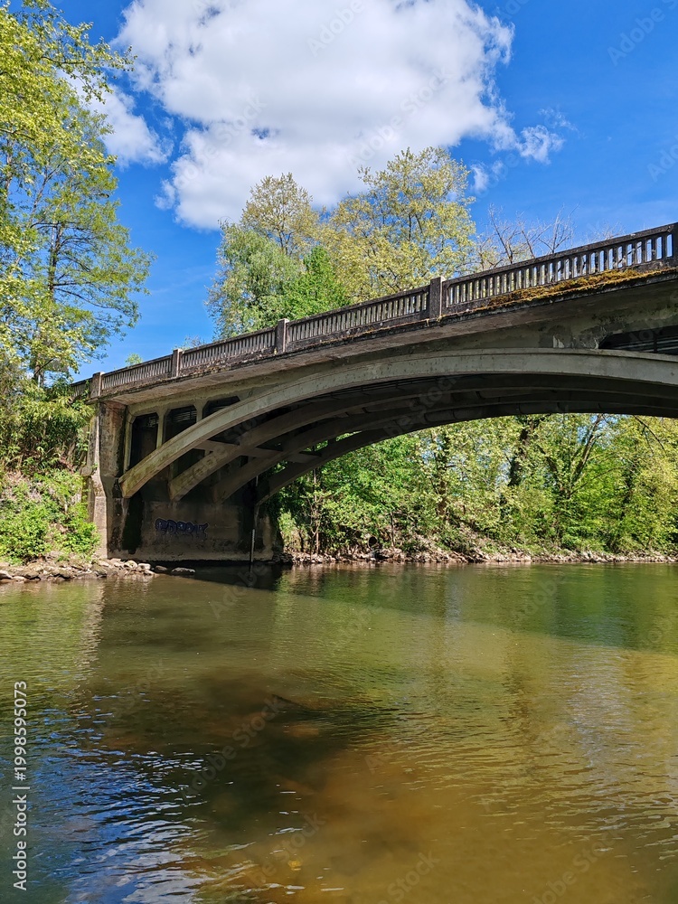 Fototapeta premium Stone bridge crossing calm river under blue spring sky