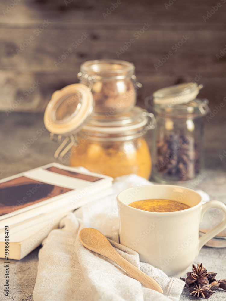 Fototapeta premium Turmeric latte golden milk with spices and books, cozy healthy lifestyle concept