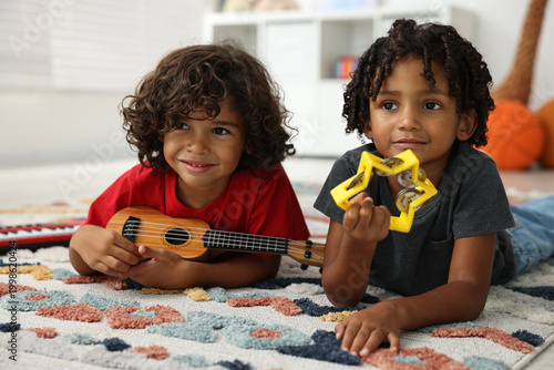 Фотография Cute little brothers playing toy musical instruments on floor at home