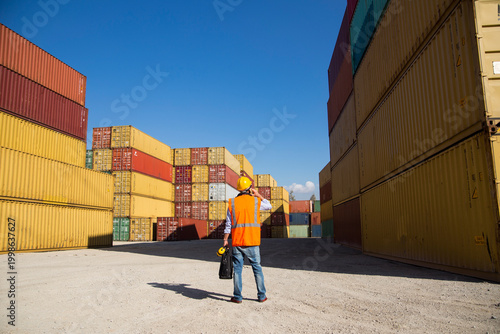 Construction worker in hard hat and safety vest operates radio at shipping container yard