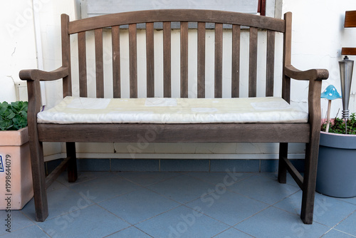 A wooden bench with a seat cushion with potted plants on both sides.