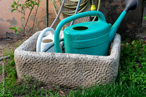 watering cans at a garden tap next to a concrete wall
