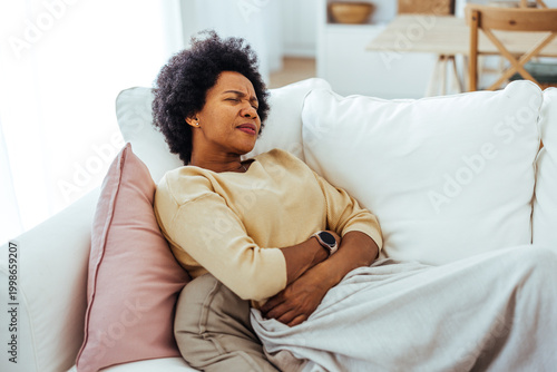 Tableau sur toile Woman Holding Stomach In Pain On Couch At Home Feeling Unwell And Experiencing A