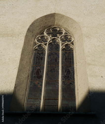 Historic Gothic Stained Glass Window with Ornate Tracery and Religious Figures in Medieval Church Wall, Authentic European Sacred Architecture Detail, Christian Art and Cathedral Heritage Background.