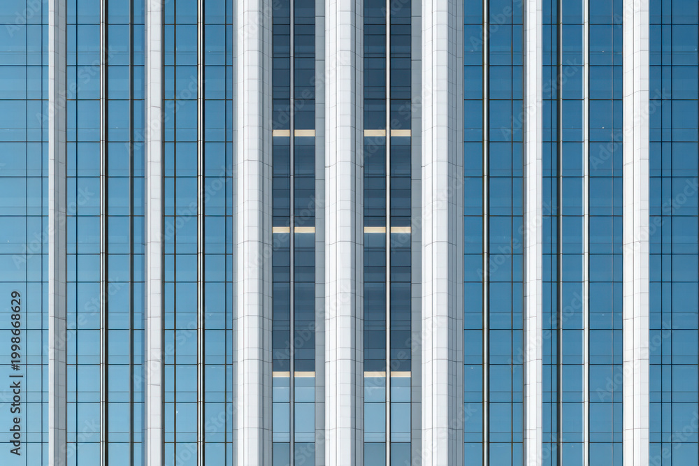 Obraz premium Modern high rise building facade with vertical glass panels and reflective surfaces, representing corporate architecture and urban development.