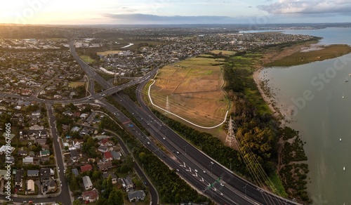 Aerial view of Auckland, New Zealand, showing the convergence of residential areas, a major highway with traffic, and the coastline.  Te Atatu South, Auckland, NZ