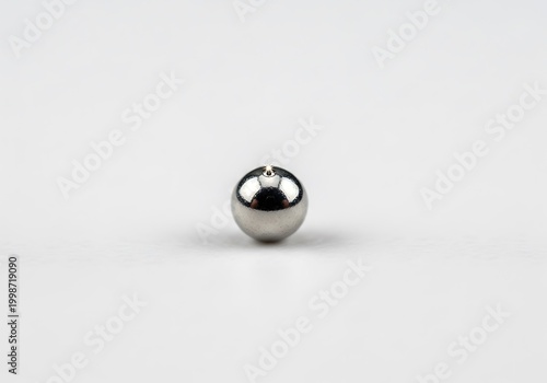 Shiny Metallic Sphere on White Surface with Minimalist Background.