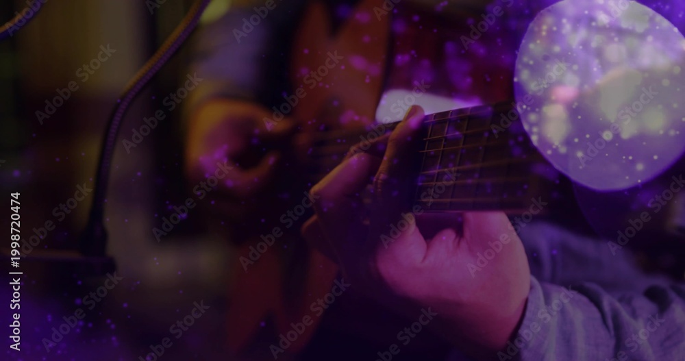 Obraz premium Playing guitarist fretting and strumming guitar in dim studio in longsleeve shirt with mic, bokeh