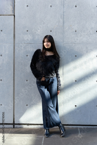 自然光で撮影したコンクリート壁の前に立つ日本人女性の全身ポートレート
