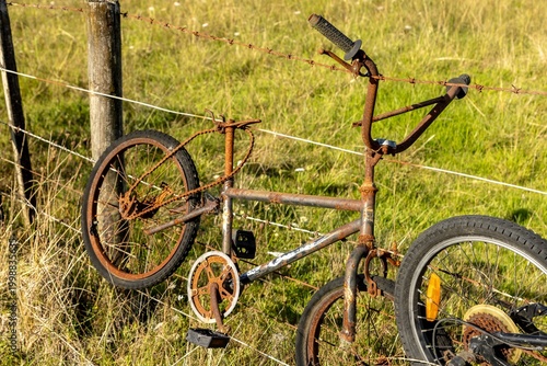 Foto A rusty, abandoned bicycle hangs on a barbed wire fence in a grassy field