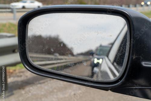 Картината върху платно Close-up of a dirty car side-view mirror reflecting a blurred highway scene with oncoming traffic, emphasizing challenging driving conditions and the importance of clear visibility