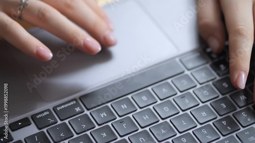 Close-up of hands typing on a laptop keyboard. Fingers press keys with precision. Touchpad area visible above keyboard. Soft lighting highlights skin and laptop surface. No animals or plants shown