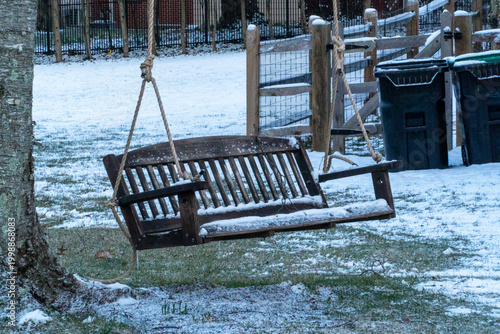 Slika na platnu Rustic wooden porch swing, dusted with a fresh layer of snow, hanging from a stu