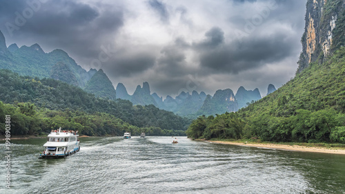 Fotografia Tourist ships and bamboo rafts float along the picturesque river