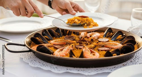 Serving delicious paella from large pan with shrimp mussels and chorizo on white plate.