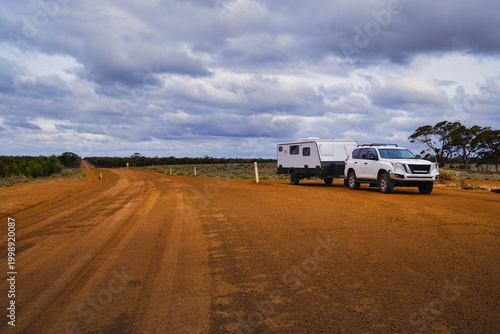 White four wheel drive towing a caravan on remote red dirt road