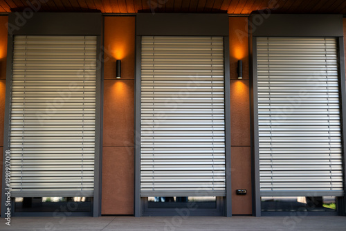 Modern building facade with external window blinds and warm evening wall lighting.