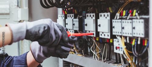Electrician technician repairing electrical control panel in industrial factory.