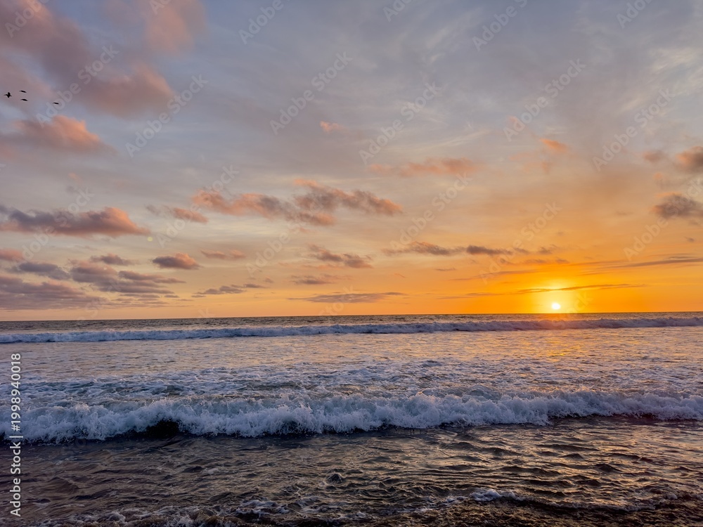 Fototapeta premium Sunset over the mighty Pacific Ocean in Carlsbad with birds in the sky and the sun setting on the right.