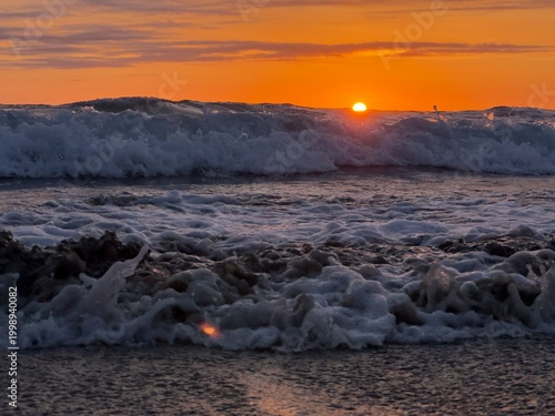 Φωτογραφία The restless and churning sea under an orange sky with the sun on the horizon in Carlsbad