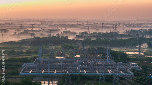 Obraz na plátně Aerial view of a high voltage substation and sprawling power transmission towers over a misty rural landscape at sunrise, with soft warm morning light