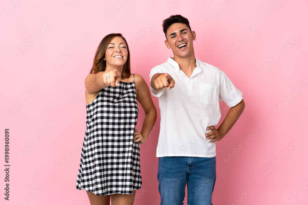 Naklejka premium Young caucasian couple isolated on pink background points finger to the front