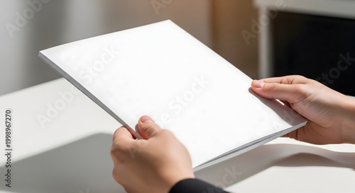 A person holds a blank white book or brochure, showcasing a clean, minimalist design ideal for mockups and presentations.