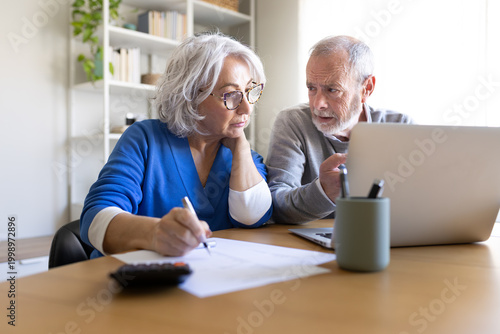 Senior couple doing home finances using laptop and calculator