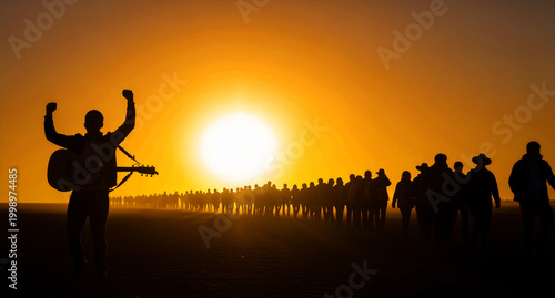 Musician silhouette with guitar raising arms against a massive orange sunset. A large crowd follows behind on a desert horizon. Hopeful leadership and spiritual journey concept for media.